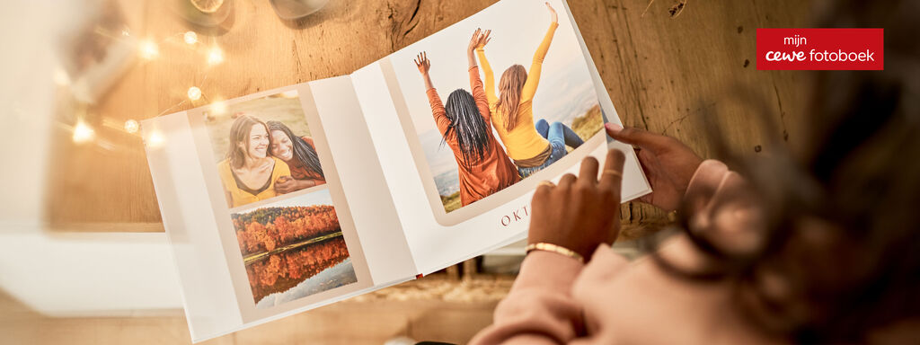 Iemand bladert door een CEWE FOTOPRODUCT met vriendenfoto’s aan een gezellige tafel.